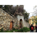 Il portale in pietra in posizione prospettica. Ai lati proseguono due mura, anch' esse in pietra. La porta è chiodata in ferro e sopra è presente una cornice, oltre la quale si trova un'edicola (Matteo Di Muro)